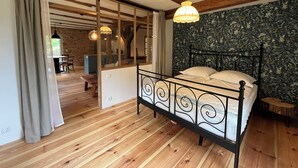 A bedroom with a wooden floor, a bed with a black metal frame, a window with curtains, and a wooden ceiling beam.