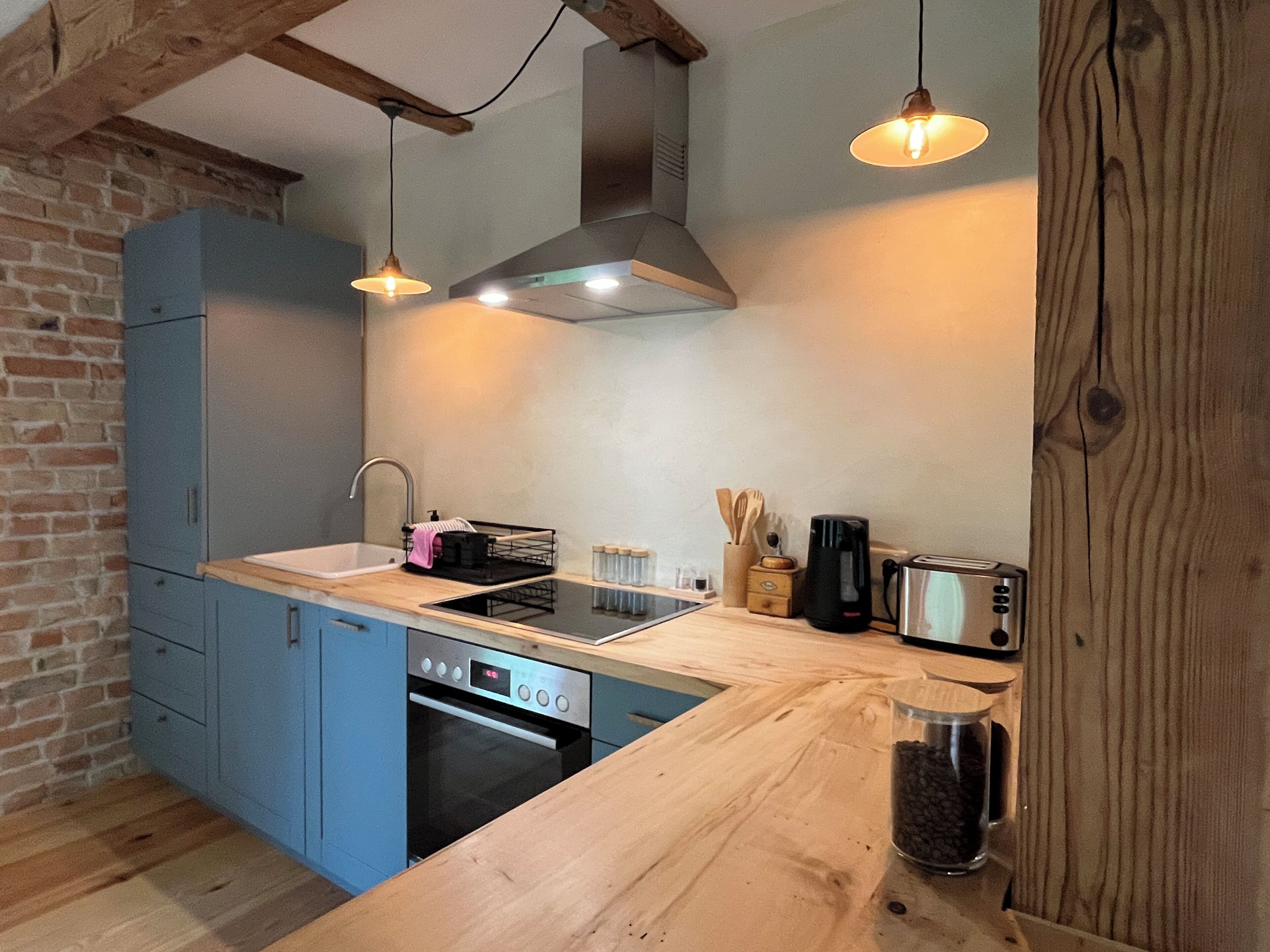 Eine Küche mit blauen Schränken, einer Holz Arbeitsplatte, einem eingebauten Backofen, einer Kaffeemaschine und einem Toaster.