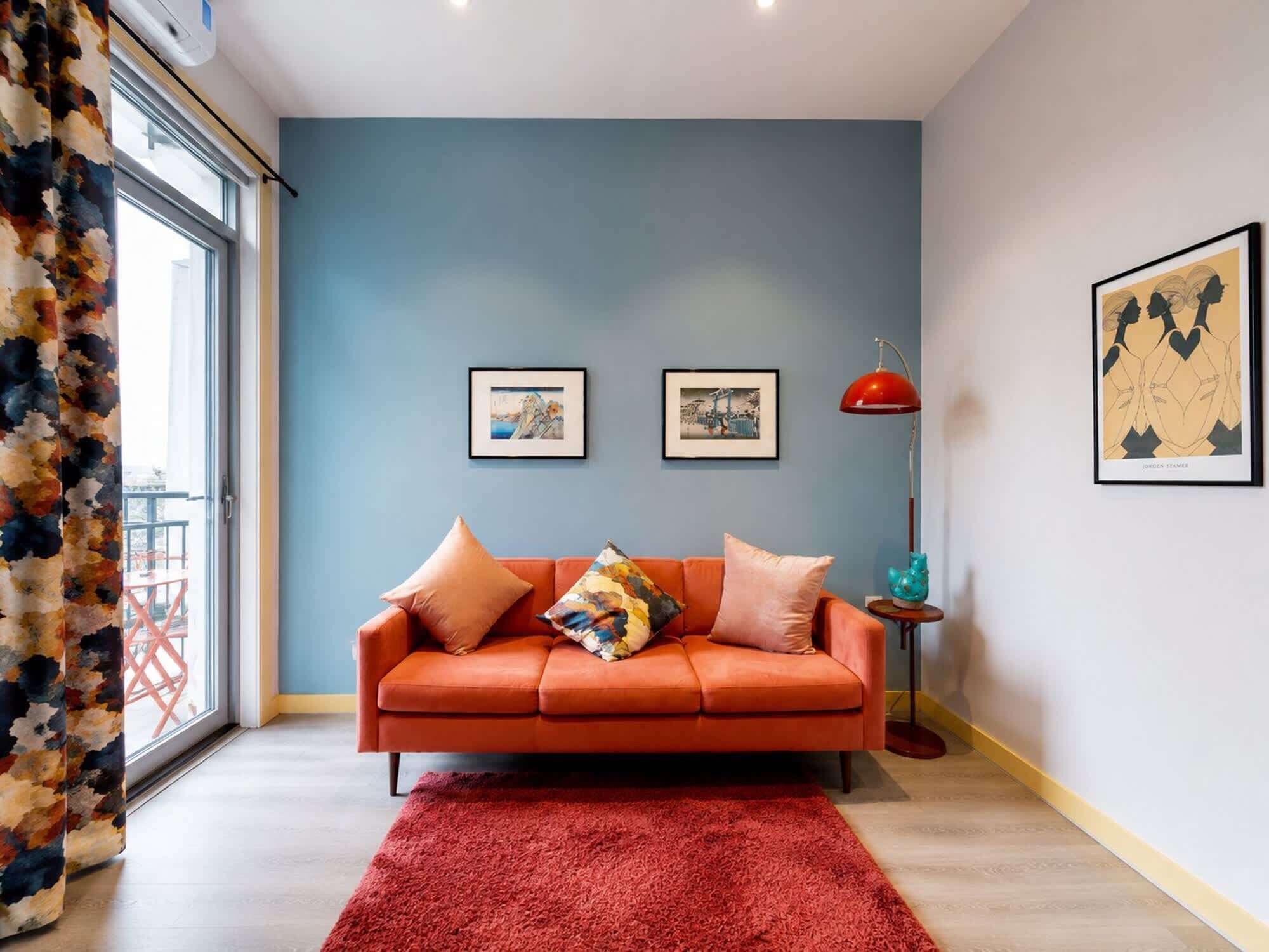 A modern living room with a sofa, two framed pictures, a red floor lamp, and a red rug.