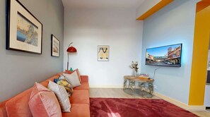 Ein Wohnzimmer mit einer Couch, einer roten Stehlampe, einem runden Couchtisch und einem flachbildfernseher an der Wand.