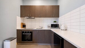 A modern kitchen with dark wooden cabinets, white tiles, a built-in oven, a microwave, and a coffee maker. - Serenity Cloud Apartment in Vibrant Footscray (Footscray)