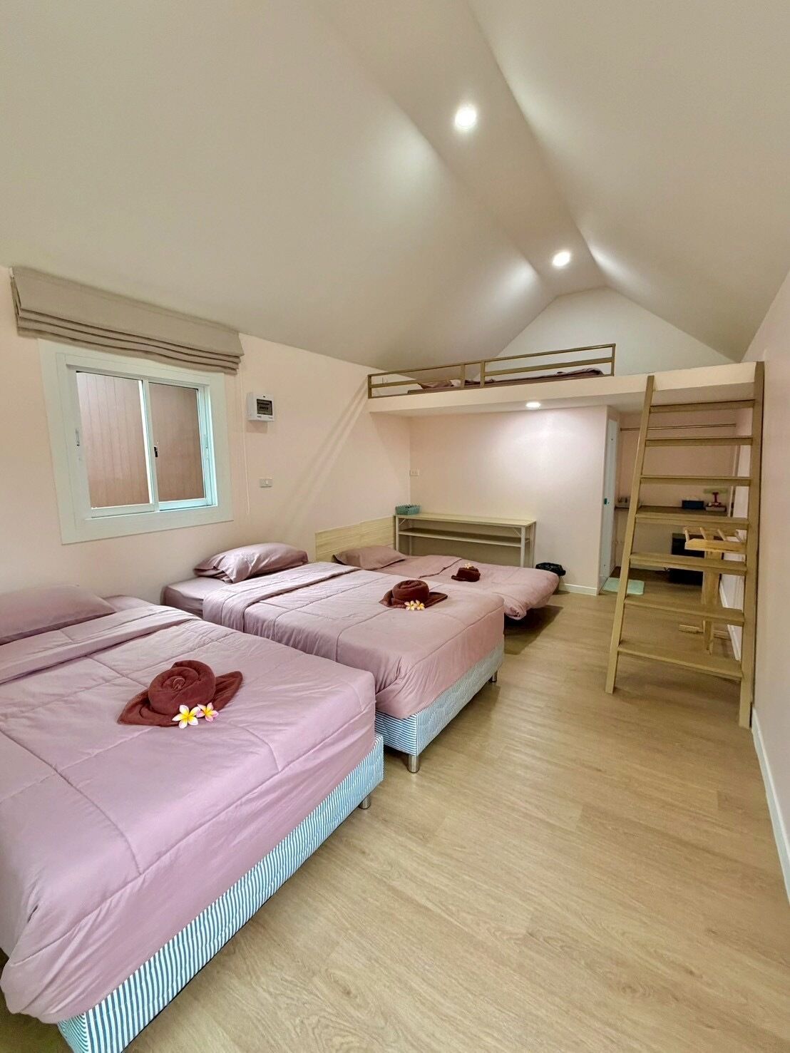 Ein Zimmer mit drei Betten, darunter einem Etagenbett, einem Fenster und einer Holzleiter.