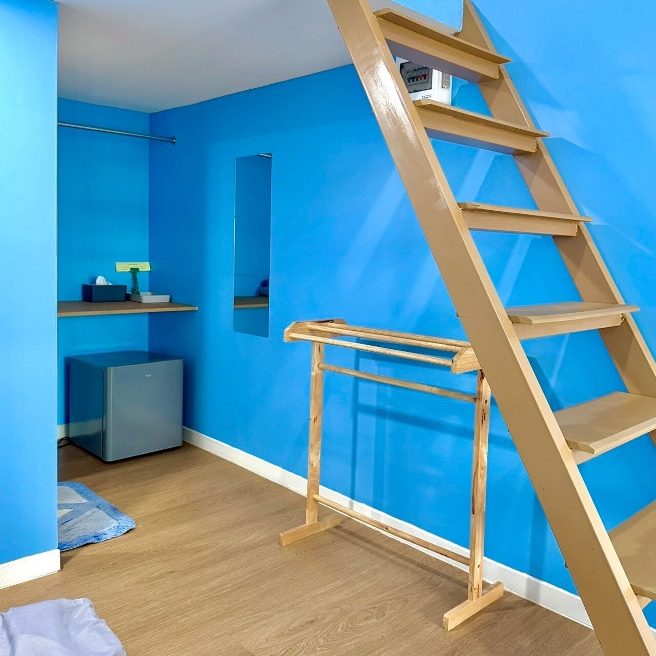 A room with a blue wall, a wooden ladder, a grey cabinet, and a small shelf with a tissue box and a plant.
