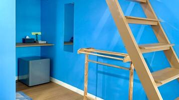 A room with a blue wall, a wooden ladder, a grey cabinet, and a small shelf with a tissue box and a plant.