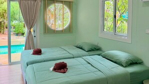 A room with two beds, an air conditioning unit, a window with a view of greenery, and a sliding glass door leading to an outdoor area. - Plumgoland (Pak Tho)