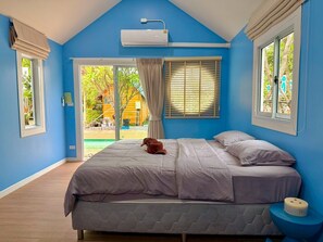 Ein Schlafzimmer mit einem Bett, einem Fenster, einer Klimaanlage und Blick auf einen Außenbereich.