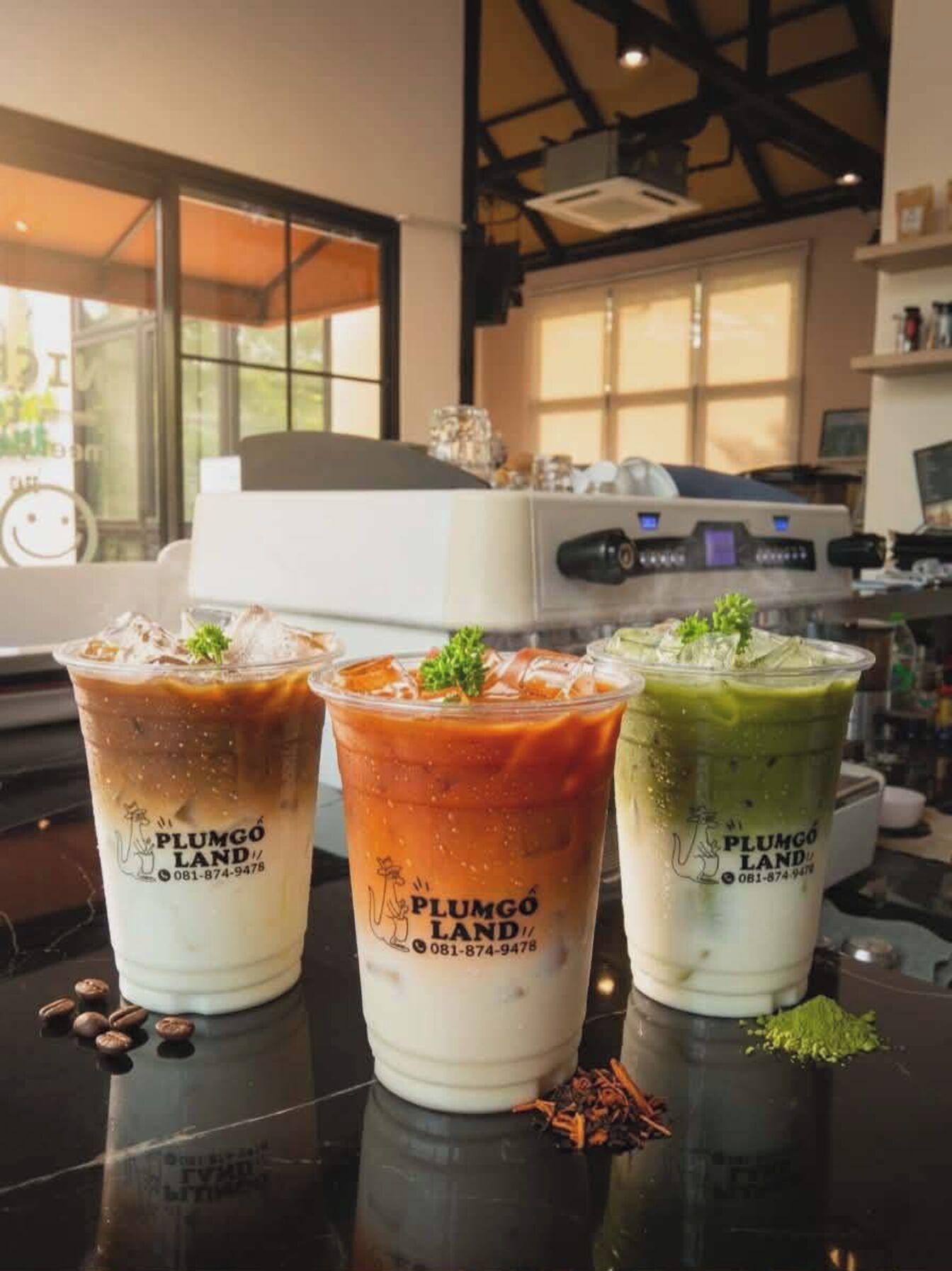Three iced drinks with a logo and a phone number on a counter in a cafe.