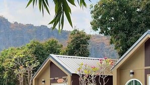 Una zona de piscina con una terraza de madera, un banco y dos edificios pequeños con ventanas circulares.
