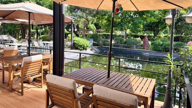 Un patio exterior con mesas y sillas de madera, sombrillas y vistas a una fuente de agua.