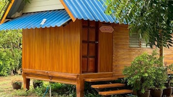 A small wooden structure with a corrugated metal roof, surrounded by potted plants and a hose.