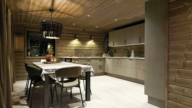 A modern kitchen with wooden paneling, a dining area with a table and chairs, and recessed ceiling lighting. - New cabin with activities and fire pit near Voss (Voss)
