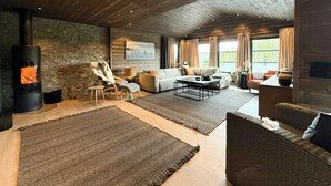 A cozy living room with a stone wall, a fireplace, a sofa, and a large rug. - New cabin with activities and fire pit near Voss (Voss)
