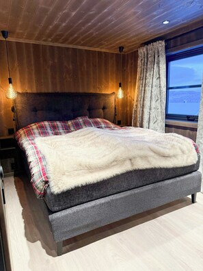 Ein Schlafzimmer mit einem großen Bett, Holzwänden, einem Fenster mit Ausblick und zwei Wandlampen.