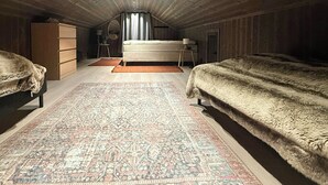 An attic bedroom with two beds, a large rug, wooden walls, and a sloped ceiling. - New cabin with activities and fire pit near Voss (Voss)