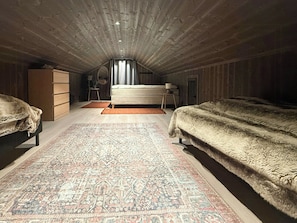 An attic bedroom with two beds, a large rug, wooden walls, and a sloped ceiling. - New cabin with activities and fire pit near Voss (Voss)