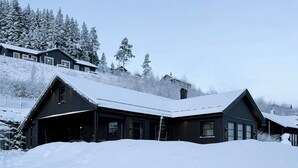 A snow-covered lodge with a large garage and a mountain backdrop. - New cabin with activities and fire pit near Voss (Voss)