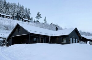 A snow-covered lodge with a large garage and a mountain backdrop. - New cabin with activities and fire pit near Voss (Voss)