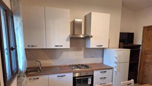 Une cuisine compacte avec des meubles blancs, une cuisinière à gaz, un four encastré et un réfrigérateur.