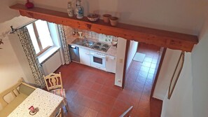 Een keuken met een fornuis, oven en wastafel, een eethoek met een tafel en stoel, en een raam met gordijnen.