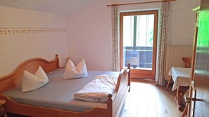 Een slaapkamer met een houten bed, een klein tafeltje en uitzicht door een raam met gordijnen.
