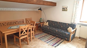 Ein Wohnzimmer mit einem Holzesstisch, vier Stühlen, einem gemusterten Sofa, einem farbenfrohen Streifen Teppich, einer Stehlampe und einem gerahmten Bild an der Wand.