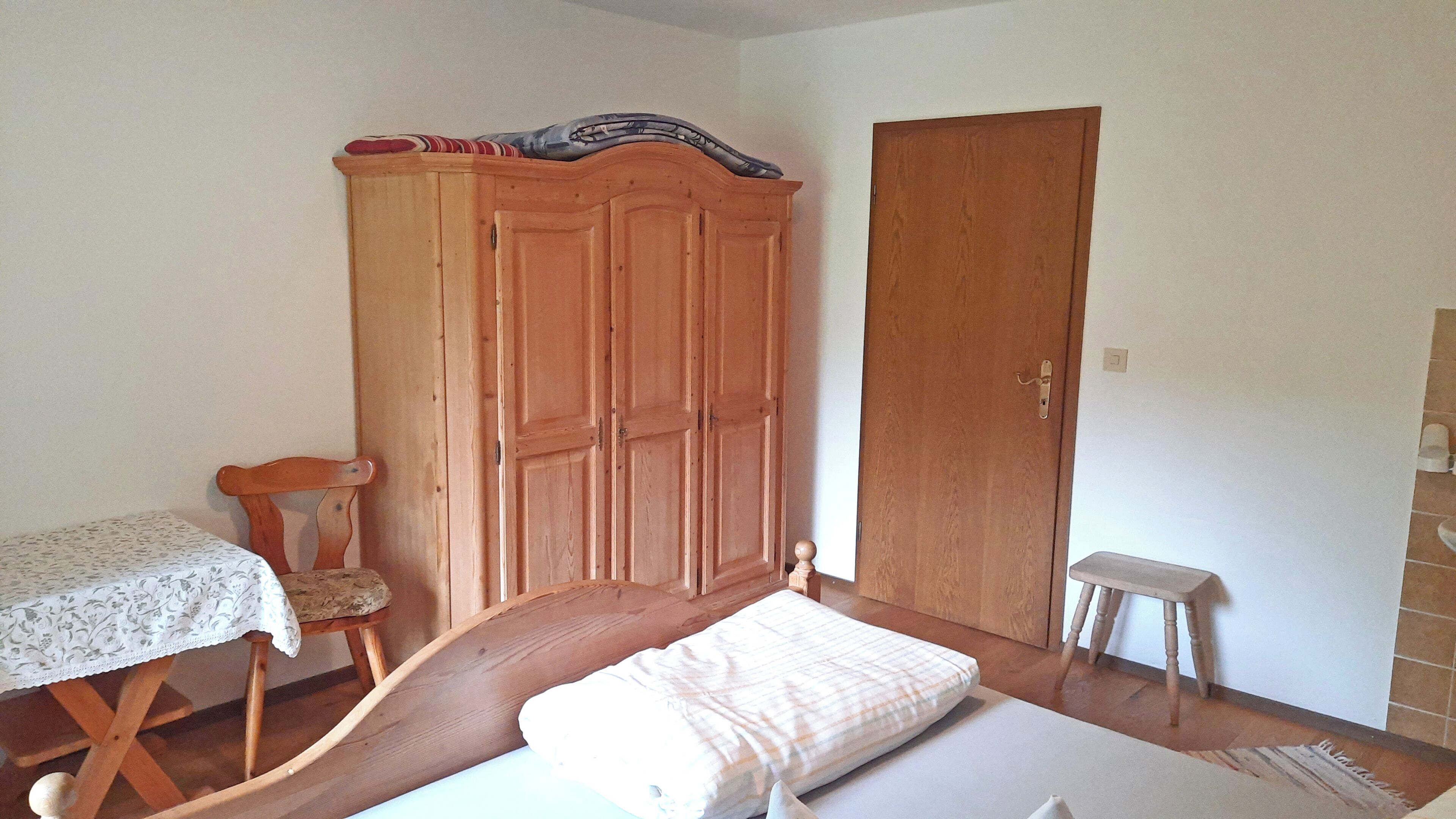 Un dormitorio con una cama, un armario de madera, una silla y una mesita.