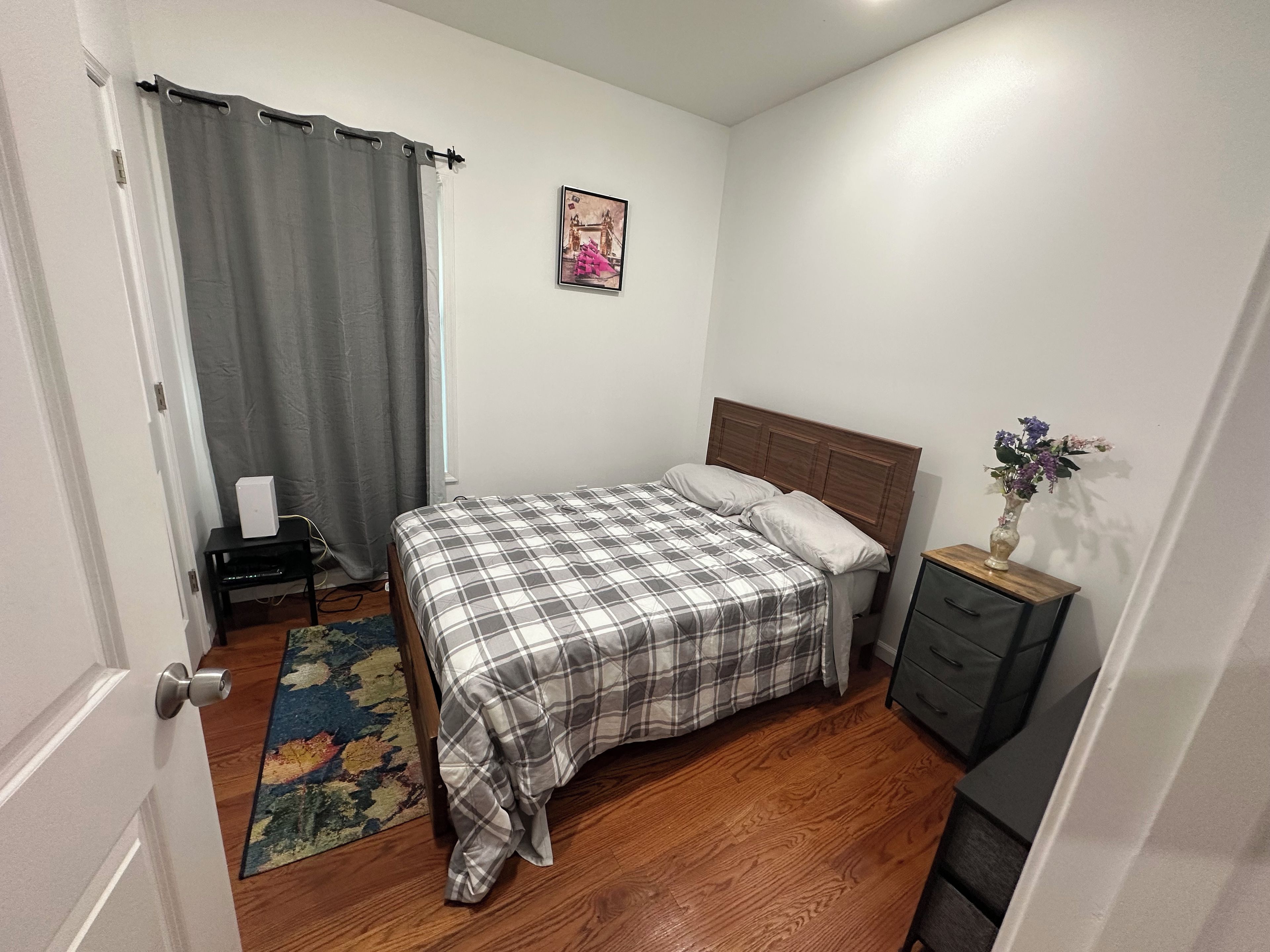 A bedroom with a bed, a nightstand, a dresser, a window with curtains, and a rug.