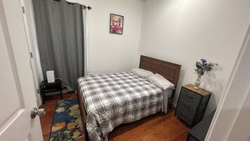 A bedroom with a bed, a nightstand, a dresser, a window with curtains, and a rug.