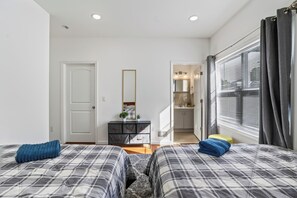 A bedroom with two beds, a dresser, a mirror, and a window with curtains.