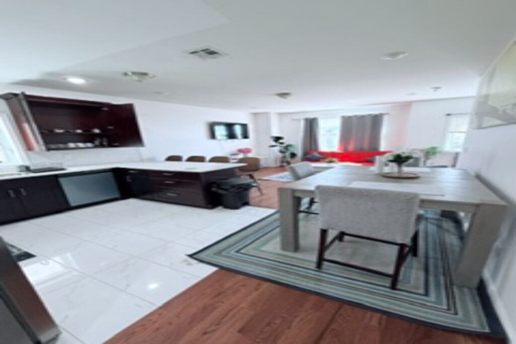 A modern kitchen with dark cabinets, a dining area with a table and chairs, and a living space with a sofa and a TV.