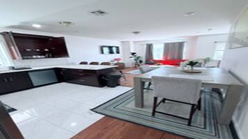 A modern kitchen with dark cabinets, a dining area with a table and chairs, and a living space with a sofa and a TV.