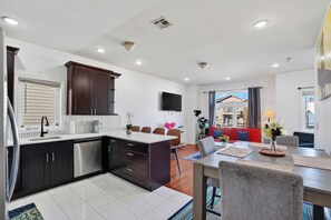 A modern kitchen with dark cabinetry, a dishwasher, and a dining area with a red sofa and a table set for four.