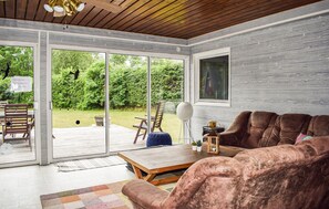 Ein gemütliches Wohnzimmer mit einer braunen Couch, einem Holztisch und einer Glastür, die auf eine Terrasse führt.