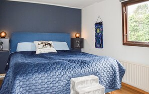 Ein Schlafzimmer mit einem großen Bett, zwei Nachttischen, einem Beistelltisch, einem Fenster mit Blick auf Bäume und einer Wandtextilie.