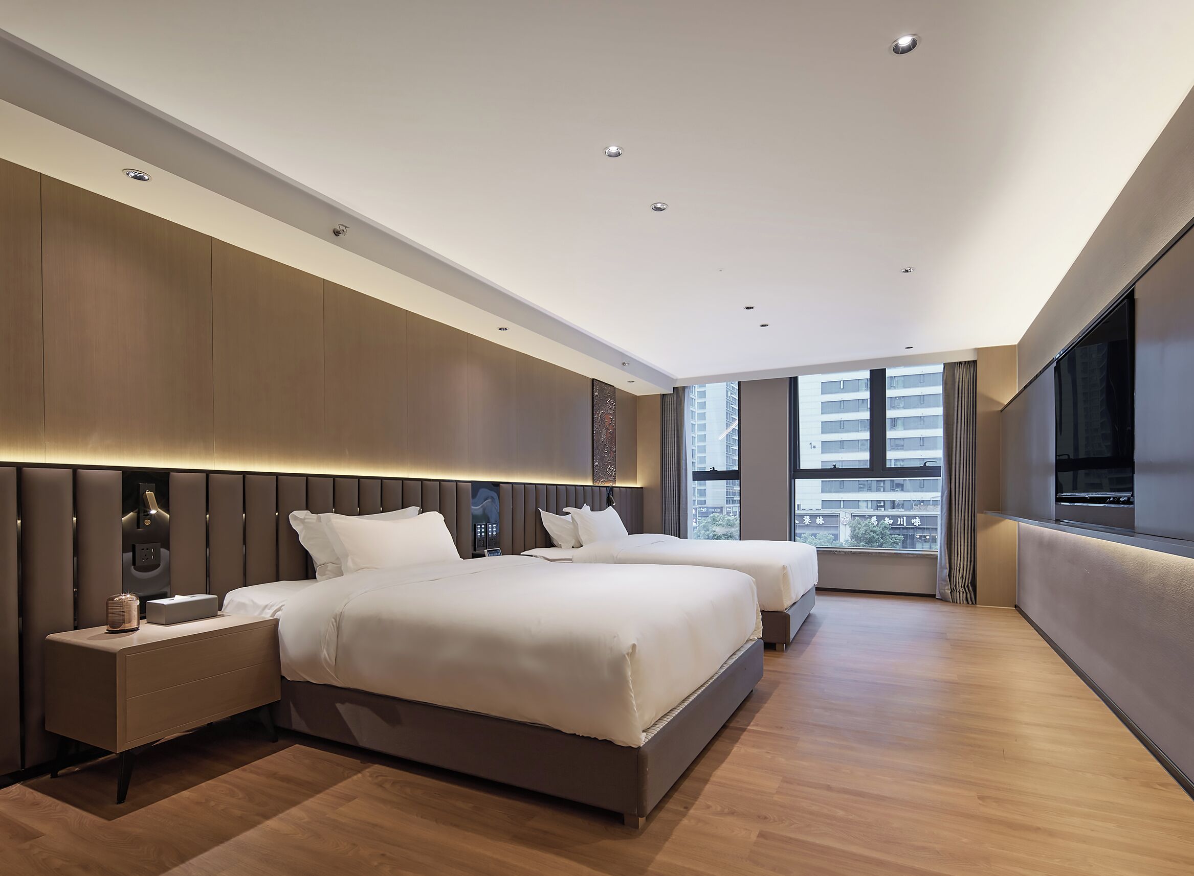 A modern hotel room with a large bed, bedside tables, a TV, and a city view.