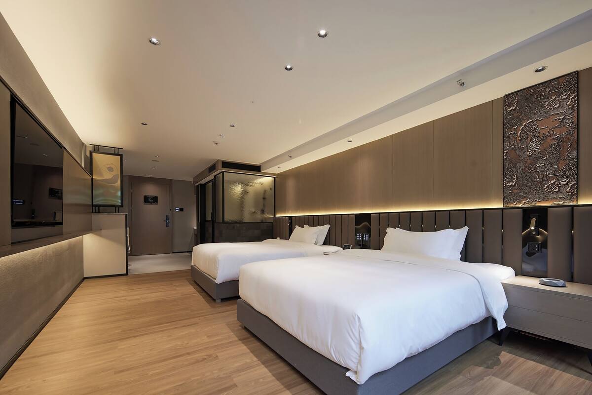 A modern hotel room with two beds, a large mirror, and a decorative wall panel.