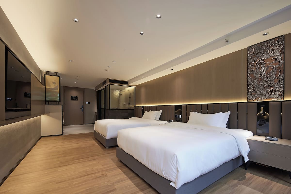 A modern hotel room with two beds, a large mirror, and a decorative wall panel.