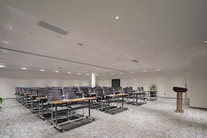 Uma sala de conferências com fileiras de cadeiras, mesas, um púlpito e piso coberto de carpete.