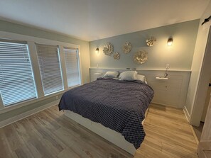 Ein Schlafzimmer mit einem Bett, zwei Nachttischen, Wandleuchten und einem Fenster mit Jalousien.