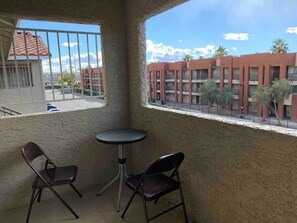 A balcony with two chairs and a small table, overlooking a building with multiple balconies and a clear sky. - Strip Area Condo, Pool, Spa & Gym Access (Las Vegas)