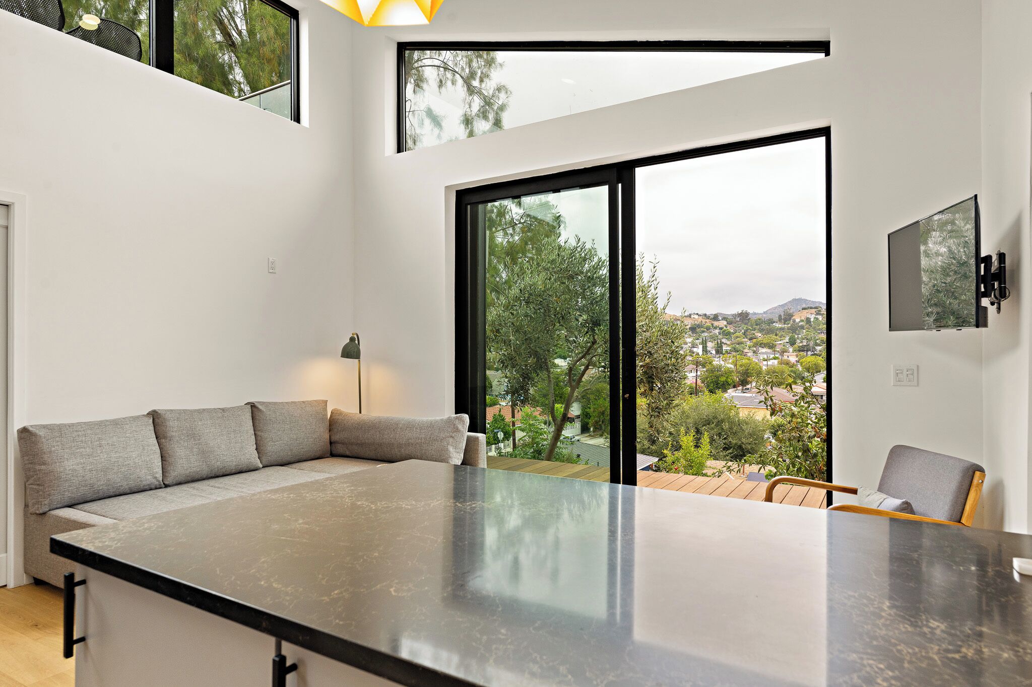 A modern kitchen with a large island, a dining area with a table and chairs, and a large sliding glass door leading to a balcony with a view of the city.