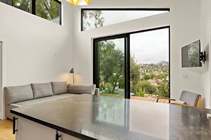 Een moderne keuken met een groot eiland, een eetruimte met een tafel en stoelen, en een grote schuifpui die leidt naar een balkon met uitzicht op de stad.