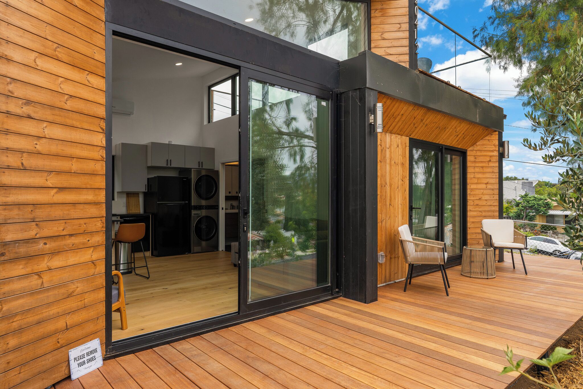 A modern house with a wooden exterior, a glass door leading to a kitchen, and a deck with outdoor seating.