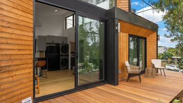 A modern house with a wooden exterior, a glass door leading to a kitchen, and a deck with outdoor seating.