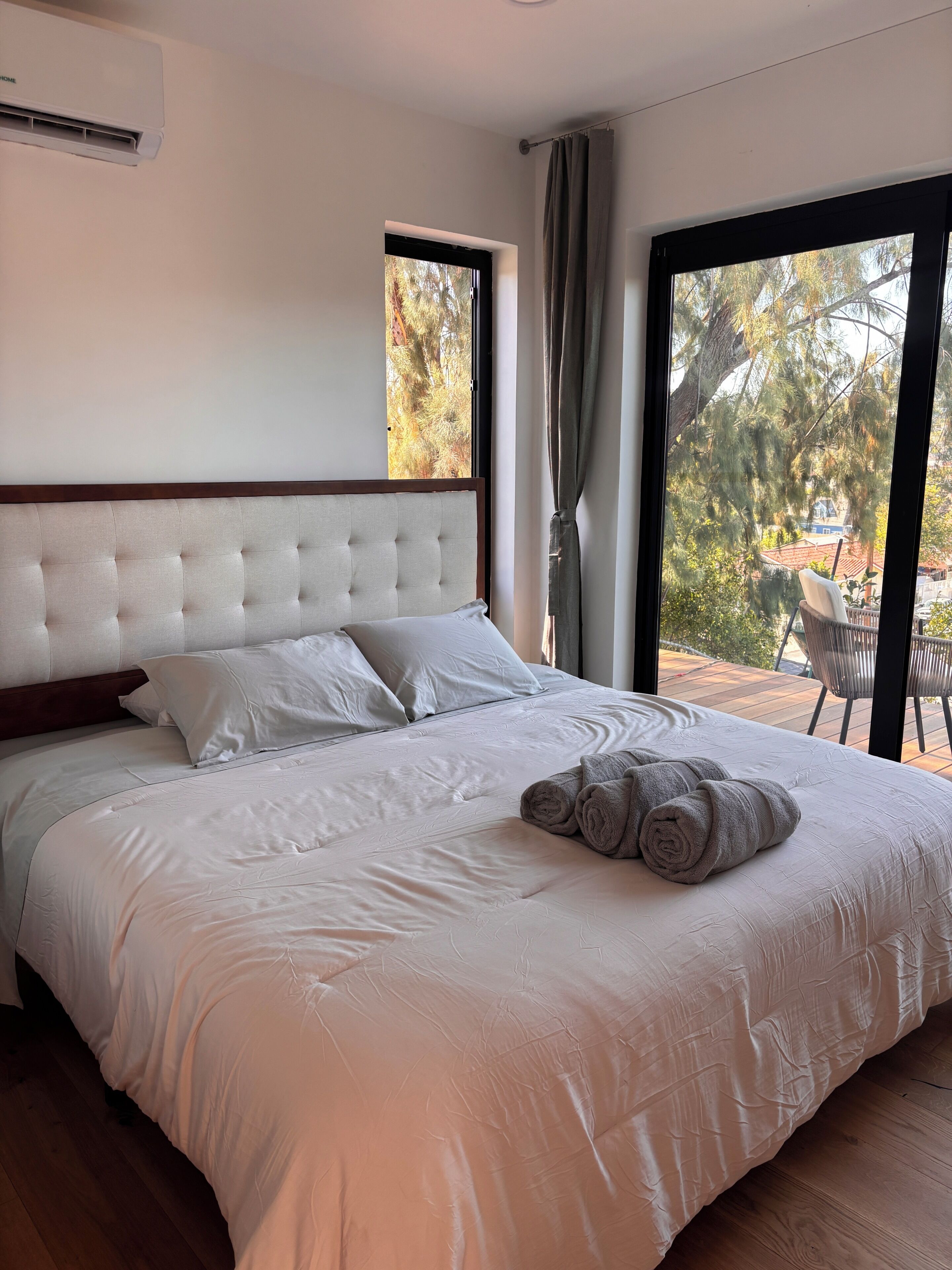A bedroom with a large bed, a window with curtains, and a view of trees and a deck outside.