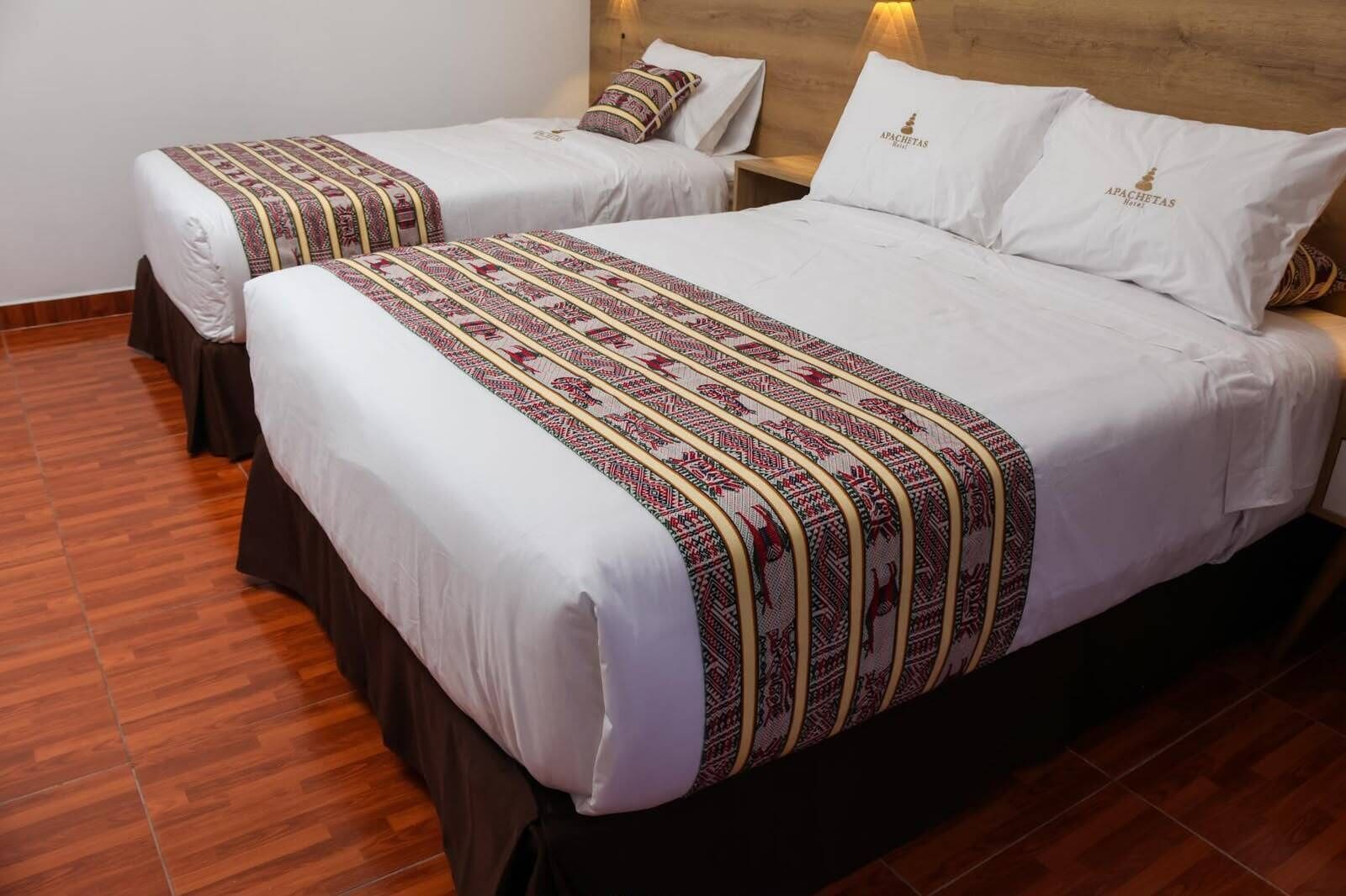 A hotel room with two beds, each with a patterned bedspread and matching pillows.