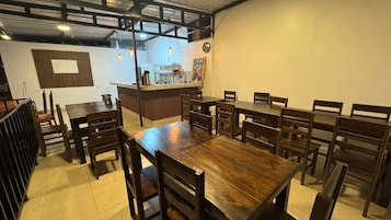 Interior de restaurante con mesas y sillas de madera, una zona de bar y un reloj en la pared.
