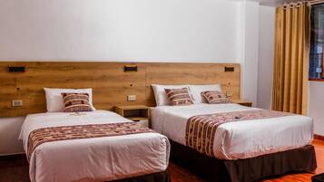Una habitación de hotel con dos camas, cabeceros de madera, ropa de cama blanca y suelo marrón.