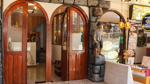La entrada de un restaurante con puertas de madera, un muro de piedra y una estatua de un hombre.