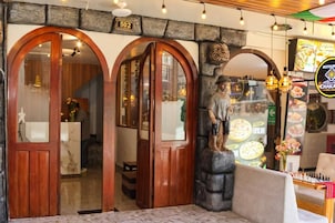 La entrada de un restaurante con puertas de madera, un muro de piedra y una estatua de un hombre.